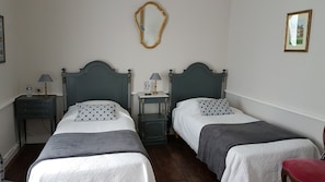 A room with two beds, each with a headboard, a bedside table, a lamp, and a mirror on the wall. - The Manoir de la Bigotière—Franz Liszt Room (Pleslin-Trigavou)