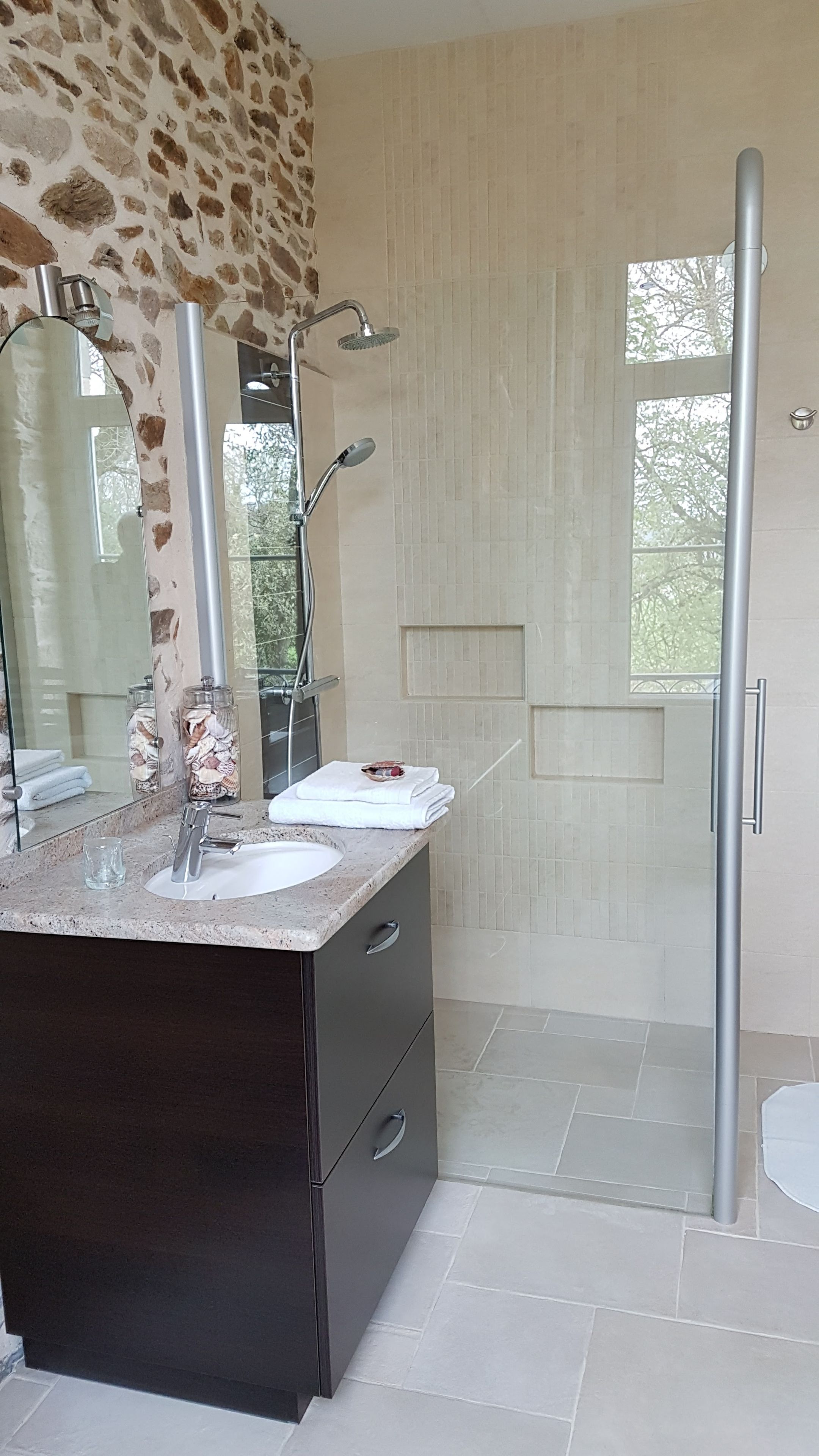 Un bagno con parete in pietra, cabina doccia in vetro e mobile lavabo con specchio.