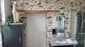 Ein Badezimmer mit Steinwand, weißer Tür, Marmorwaschbecken, Spiegel und Dusche.