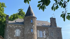 Ein Gebäude aus Stein mit einem Türmchen, mehreren Fenstern mit Fensterläden und einem geneigten Dach.