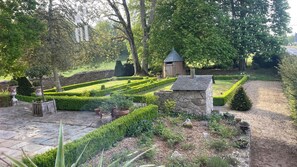 Un jardín bien cuidado con una estructura de piedra, setos recortados y una variedad de plantas.