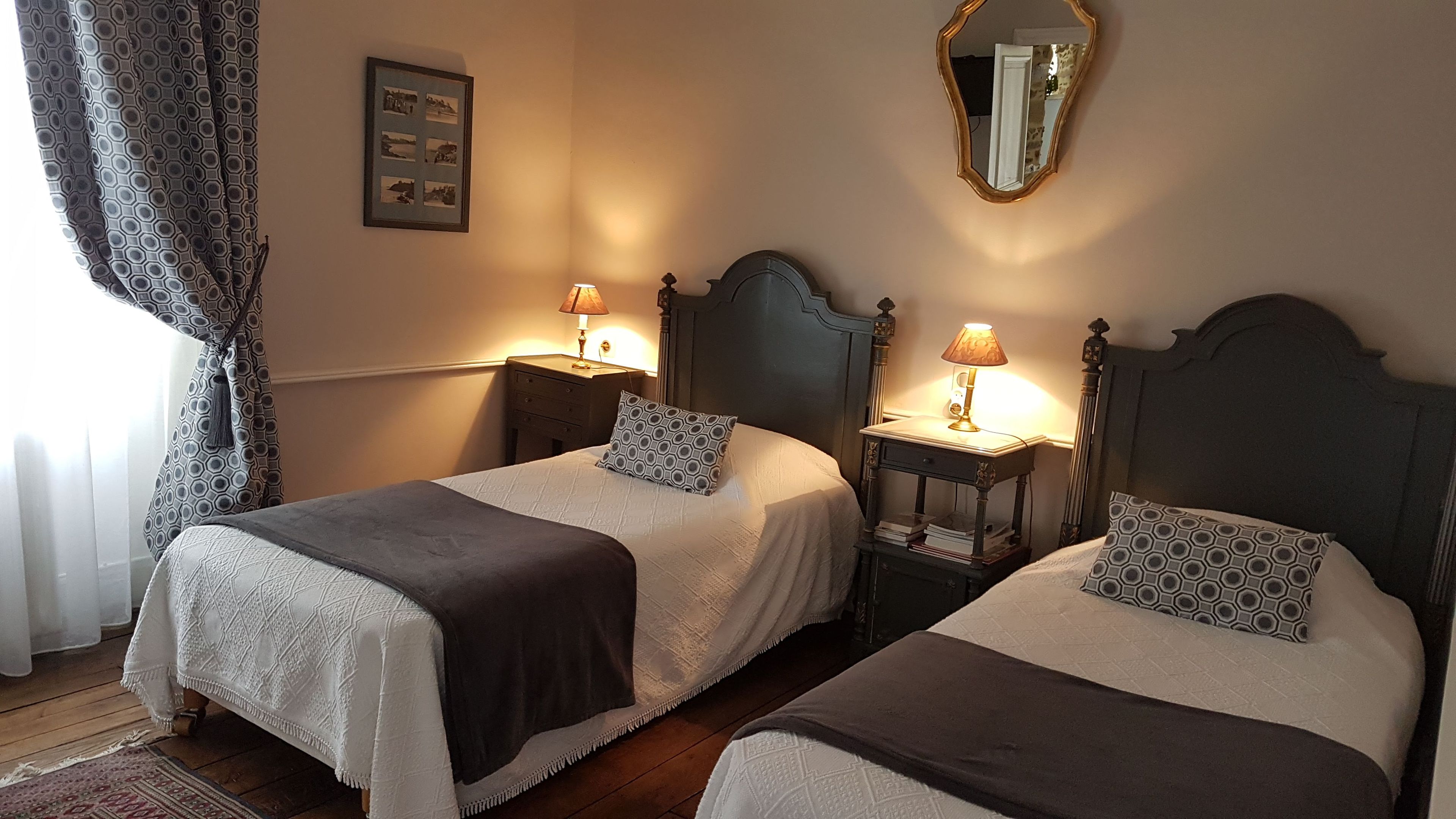 Une chambre d’hôtel avec deux lits, chacun agrémenté d’un oreiller à motifs, une table de chevet avec une lampe et un tableau encadré au mur.