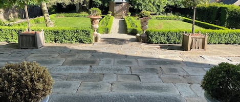 A stone pathway leading to a gated entrance surrounded by well-manicured hedges and trees.