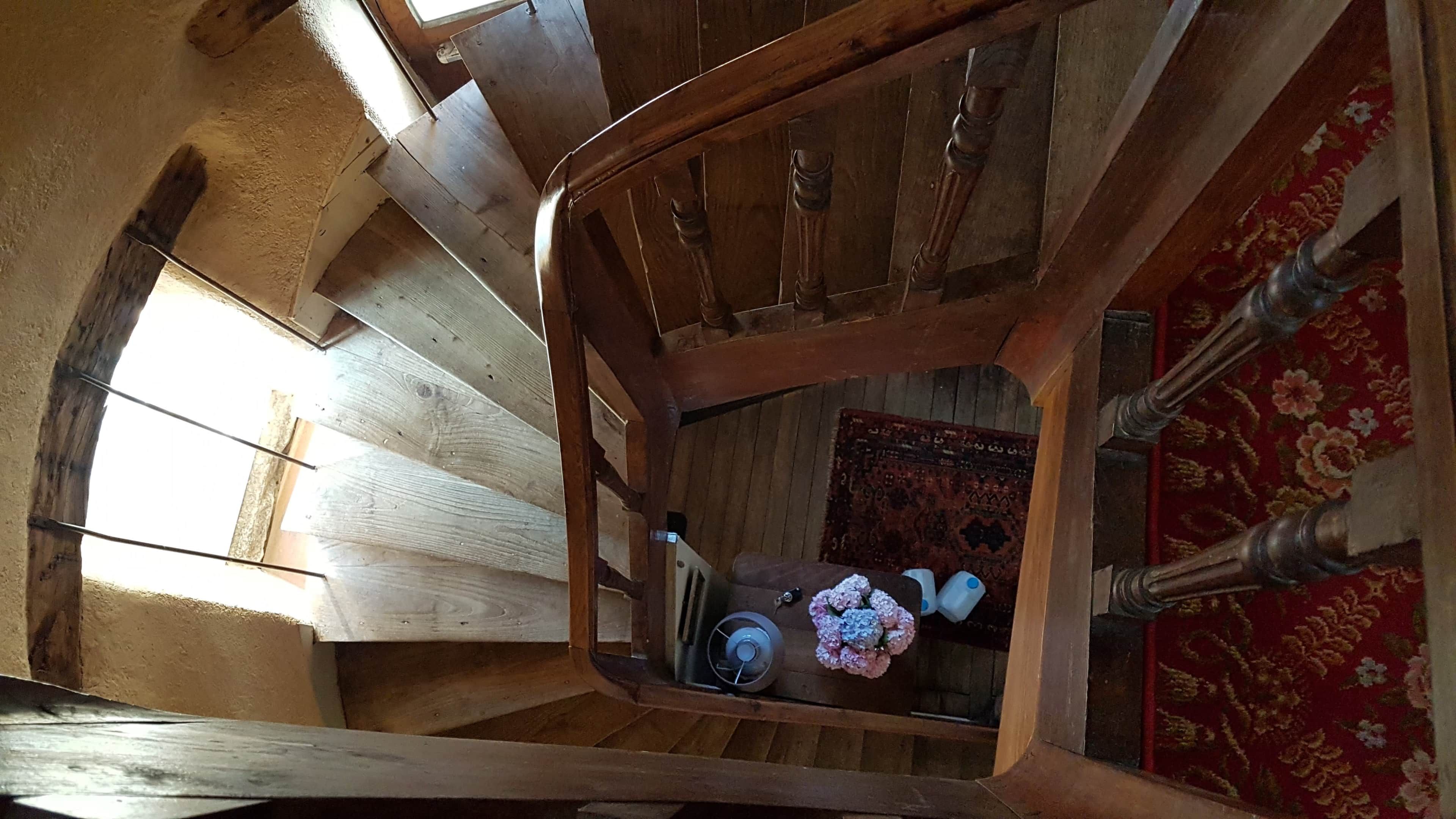 Una escalera de madera con vistas a una habitación de abajo, que incluye una alfombra estampada y una pequeña mesa con objetos encima.