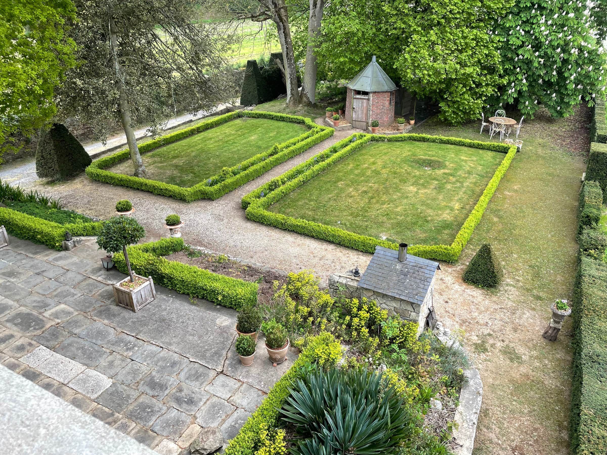 A well-maintained garden with geometric lawn patterns, a small brick structure, and a seating area.