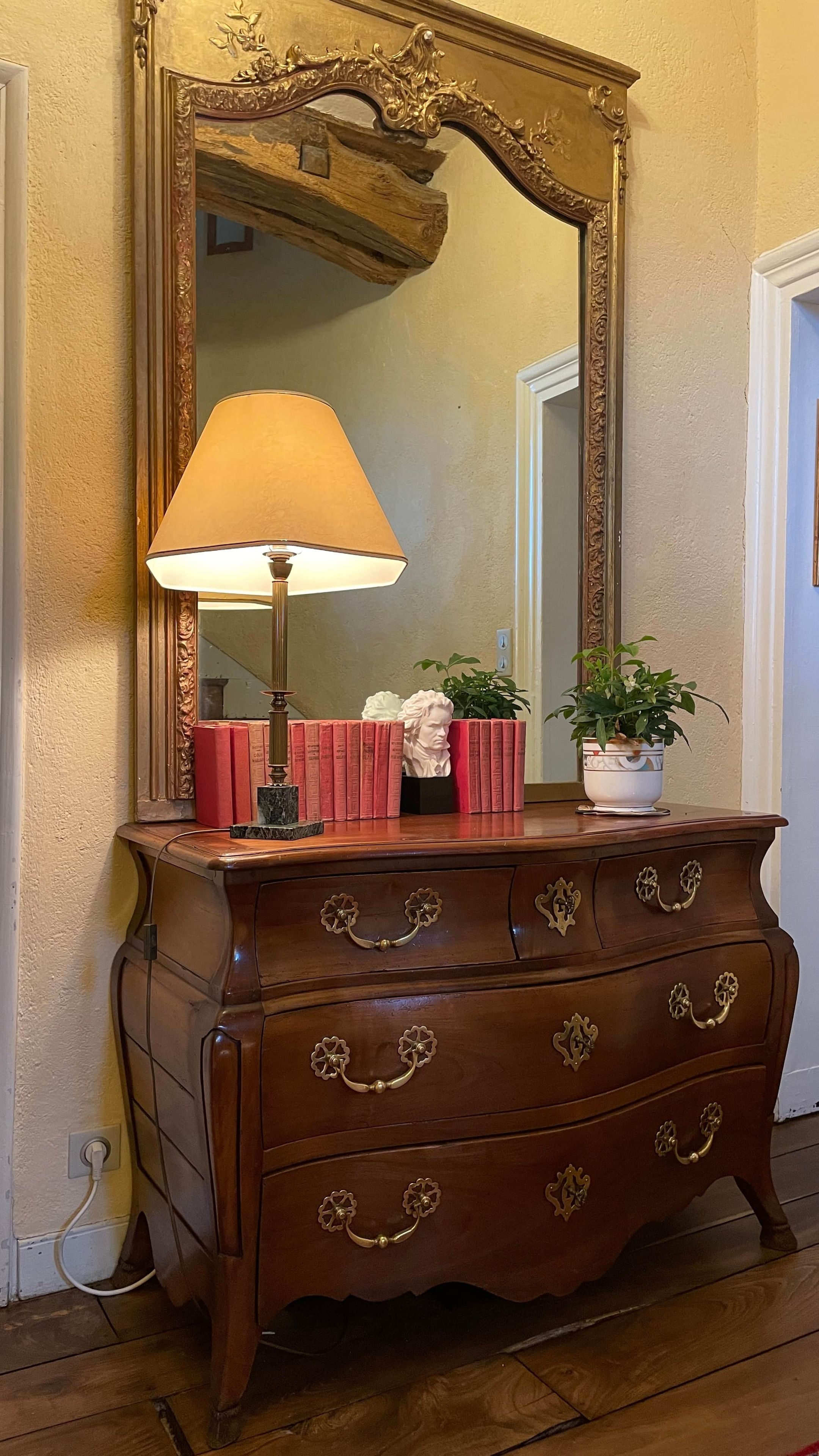Une commode en bois dotée de poignées décoratives, un miroir avec un cadre orné et une lampe.