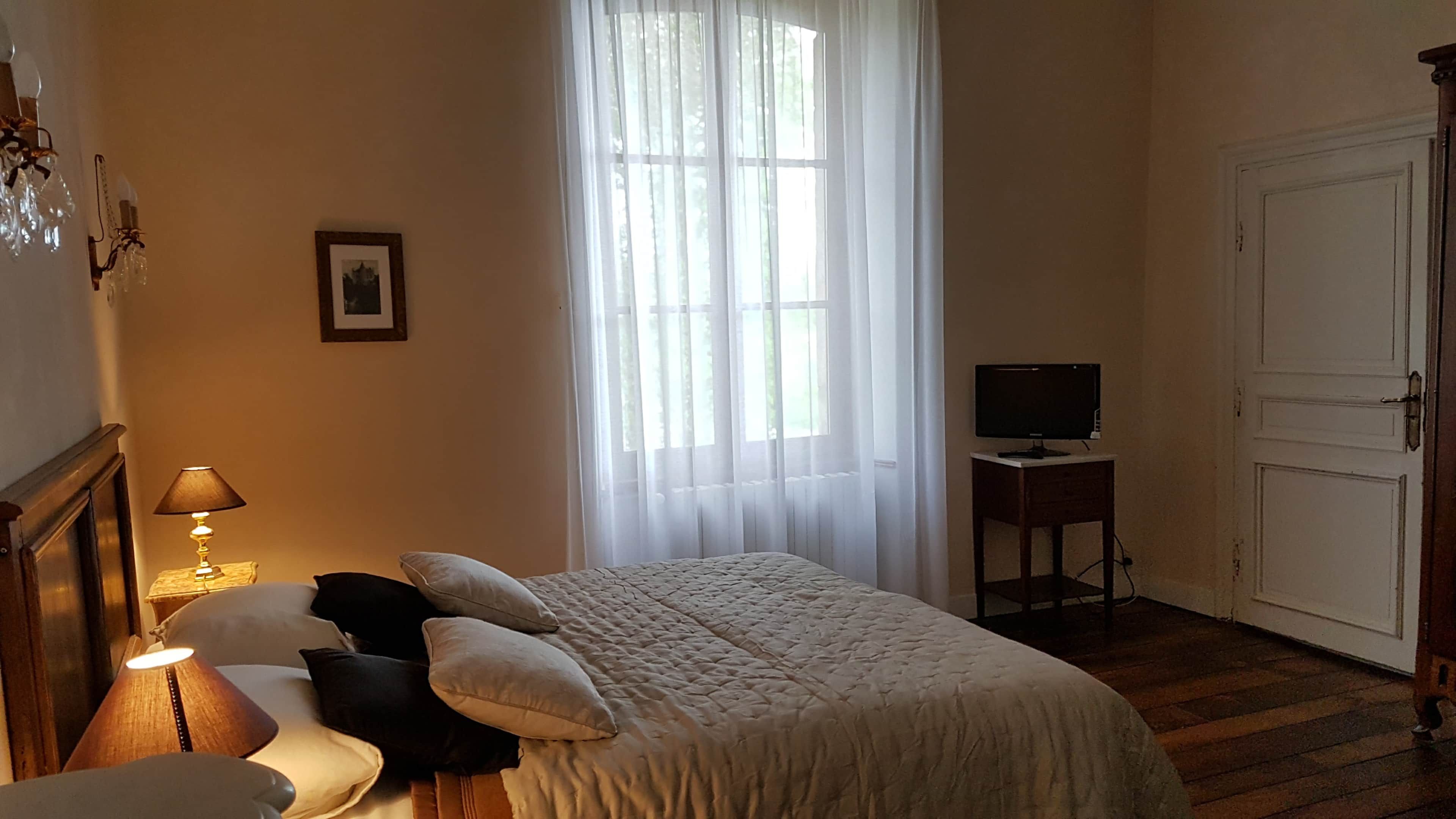 Een slaapkamer met een bed, een nachtkastje met een lamp, een televisie op een dressoir en een deur.
