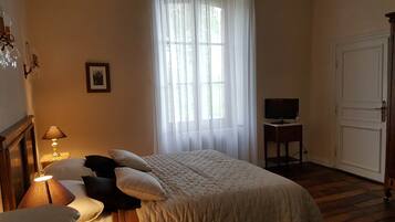 Een slaapkamer met een bed, een nachtkastje met een lamp, een televisie op een dressoir en een deur.
