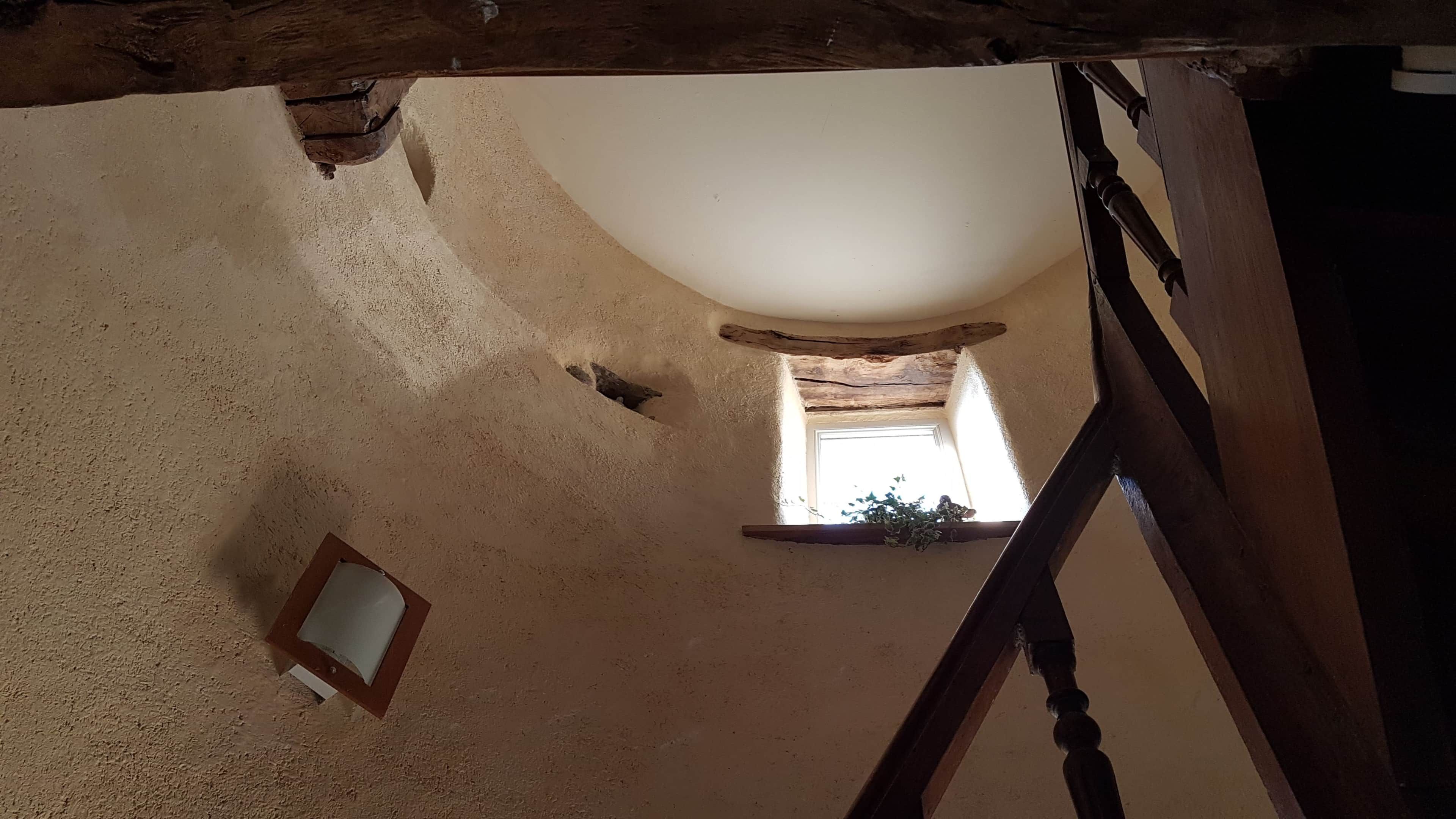 Un intérieur rustique avec un escalier en bois, une petite fenêtre offrant une vue agréable et un mur à la texture intéressante.