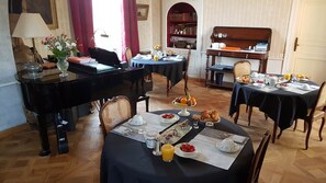 A dining area with a piano, tables set for breakfast, and a bookshelf in the background. - The Manor of Bigotière (Pleslin-Trigavou)