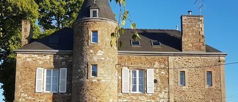 A stone building with a tower, multiple windows, and a chimney.