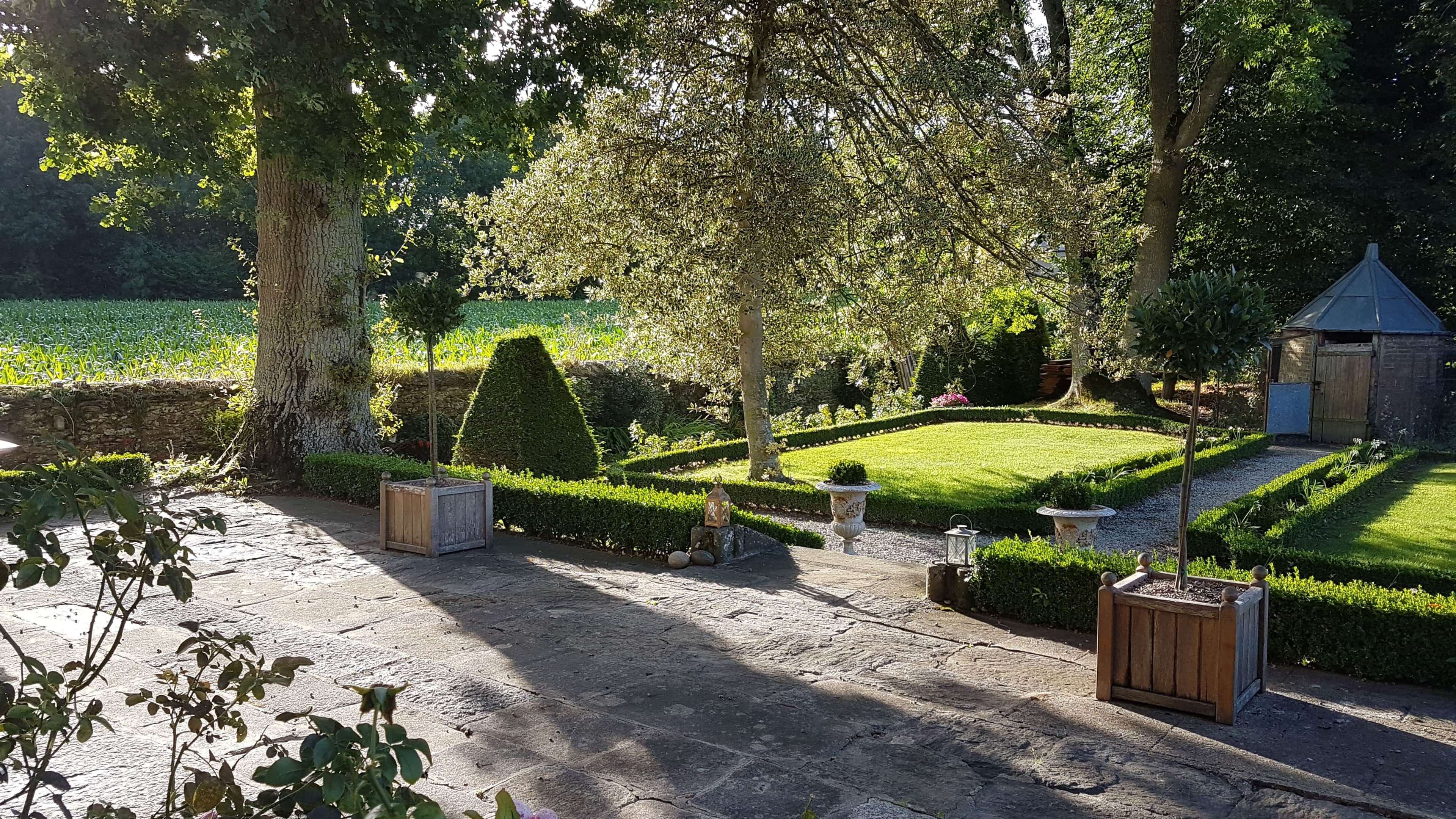 Un jardin bien entretenu, avec un chemin de pierres, des haies soigneusement taillées et une petite construction en briques.