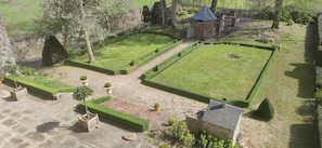 Un jardin bien entretenu, avec un chemin de pierres, des haies soigneusement taillées et une petite construction en briques.