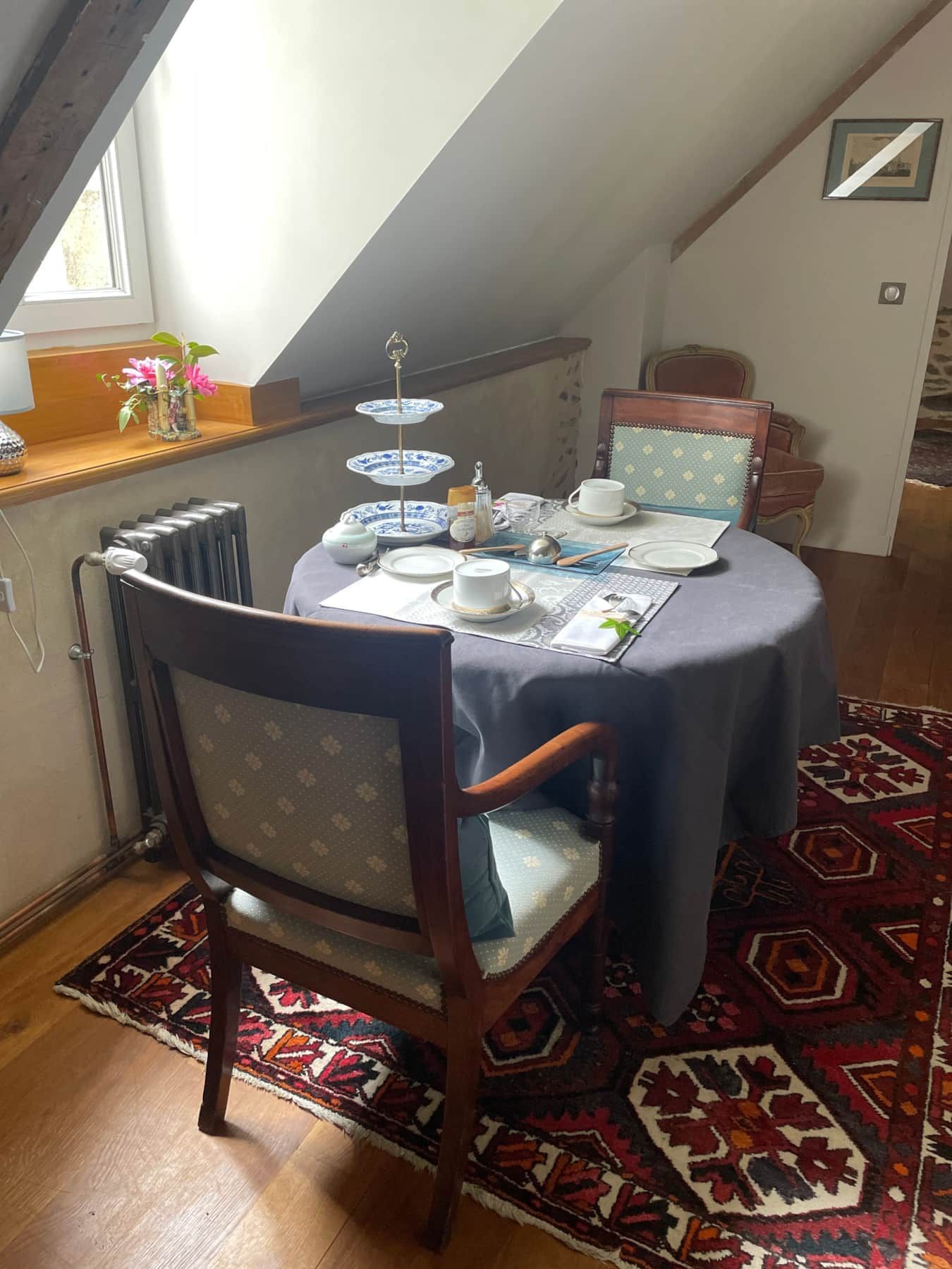 A dining area with a table set for two, a chair, a radiator, and a window.