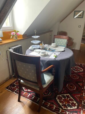 Un coin repas avec une table dressée pour deux personnes, une chaise, un radiateur et une fenêtre.