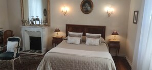 A bedroom with a large bed, two bedside tables with lamps, a fireplace, a chair, and a mirror. - The Manor of Bigotière (Pleslin-Trigavou)