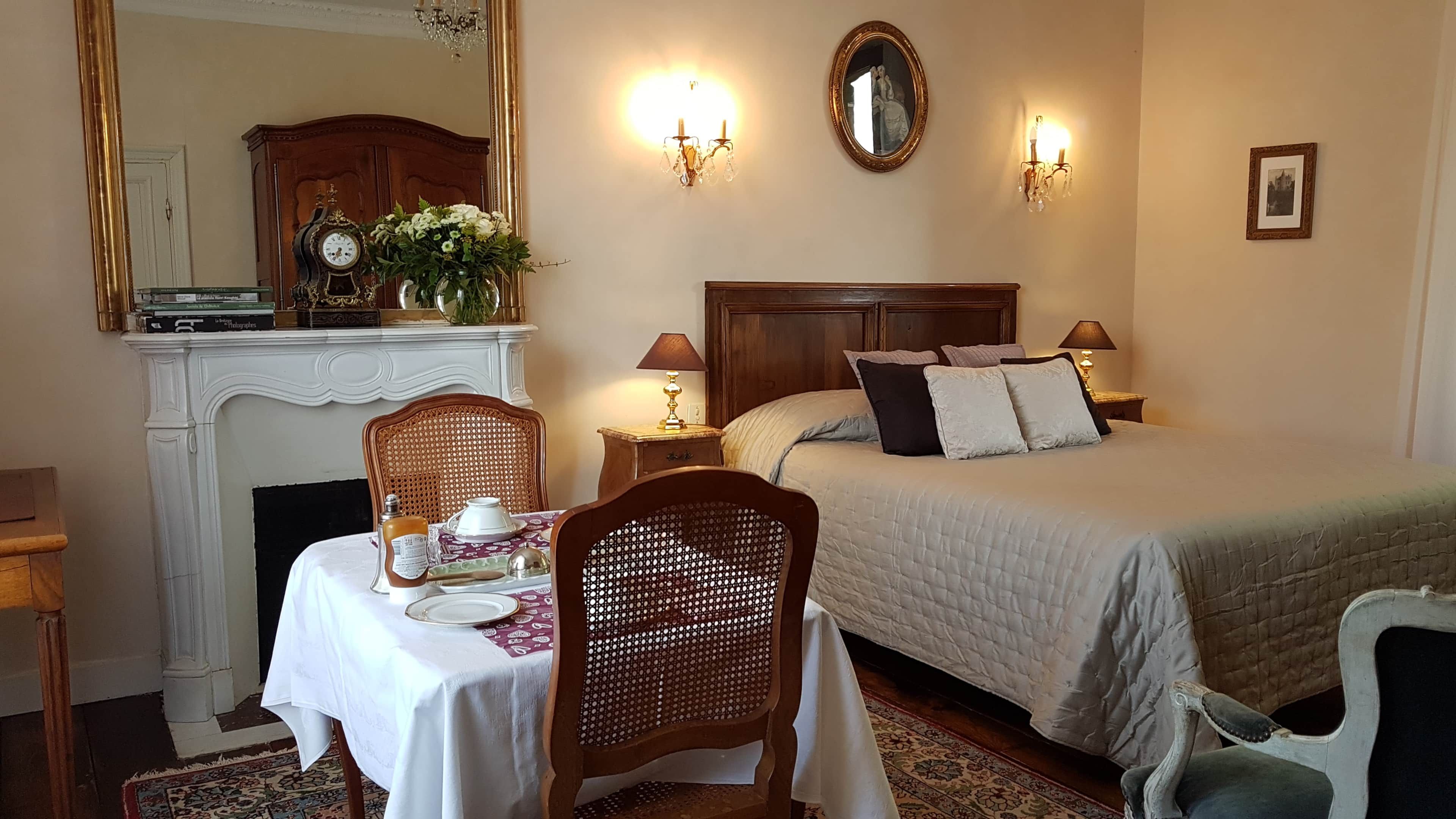 Une chambre d’hôtel comprenant un lit, des tables de chevet, un miroir, une cheminée et un coin repas avec une table et des chaises.