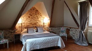 Ein Schlafzimmer mit Steinswand, einem Bett mit Kissen, einem Nachttisch, einem Sessel und einem Fenster mit Vorhängen.