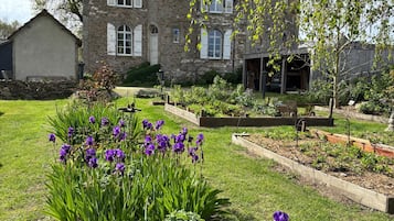 Ein Gebäude aus Stein mit einem Turm, umgeben von einem gepflegten Garten mit violetten Blumen.