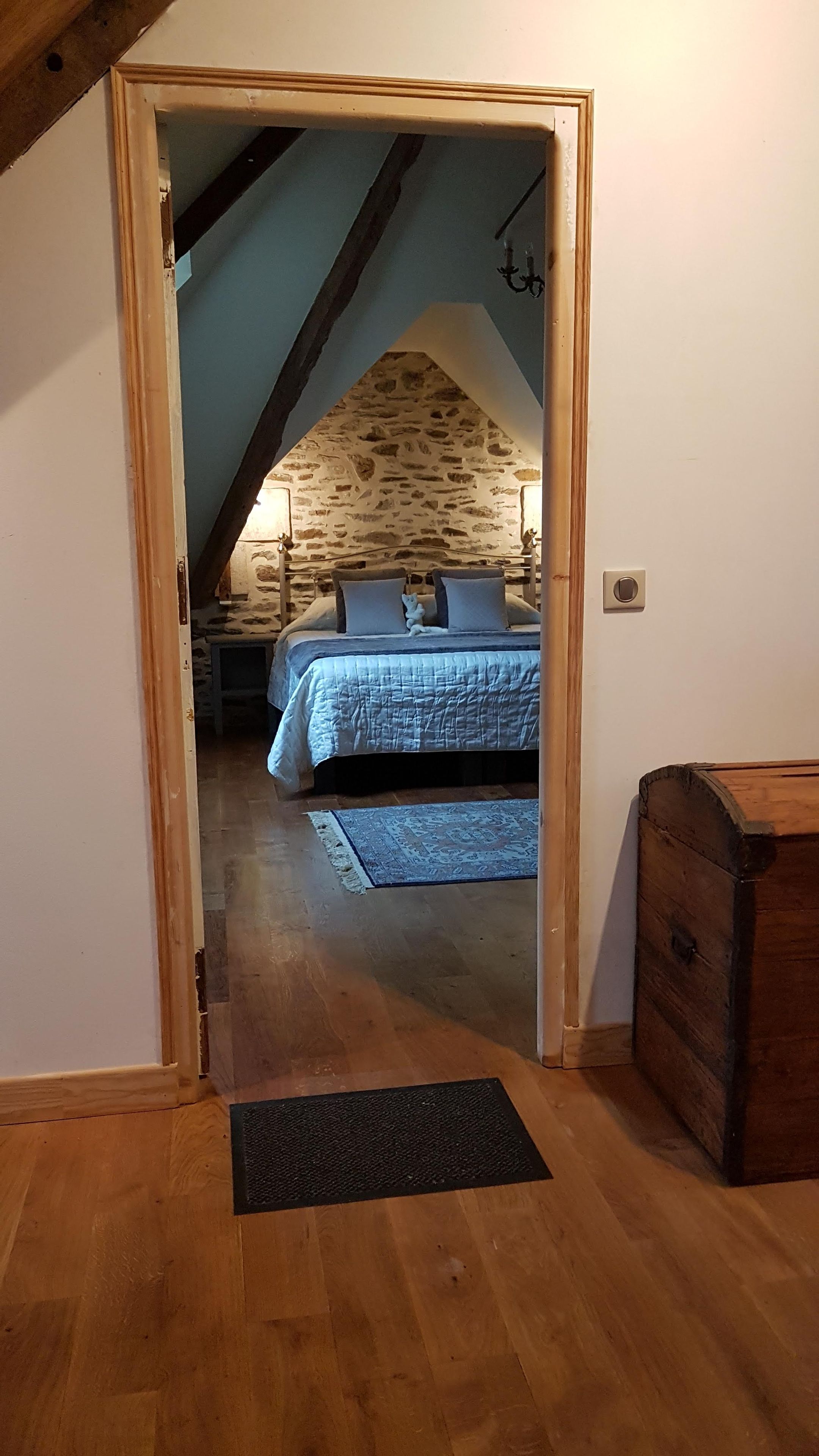 Een slaapkamer op zolder met een stenen muur, een bed met een blauwe sprei en een houten kist.