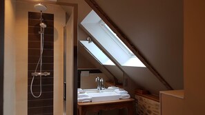 Ein Badezimmer mit Dachfenster, Dusche und Waschbecken mit Handtüchern.