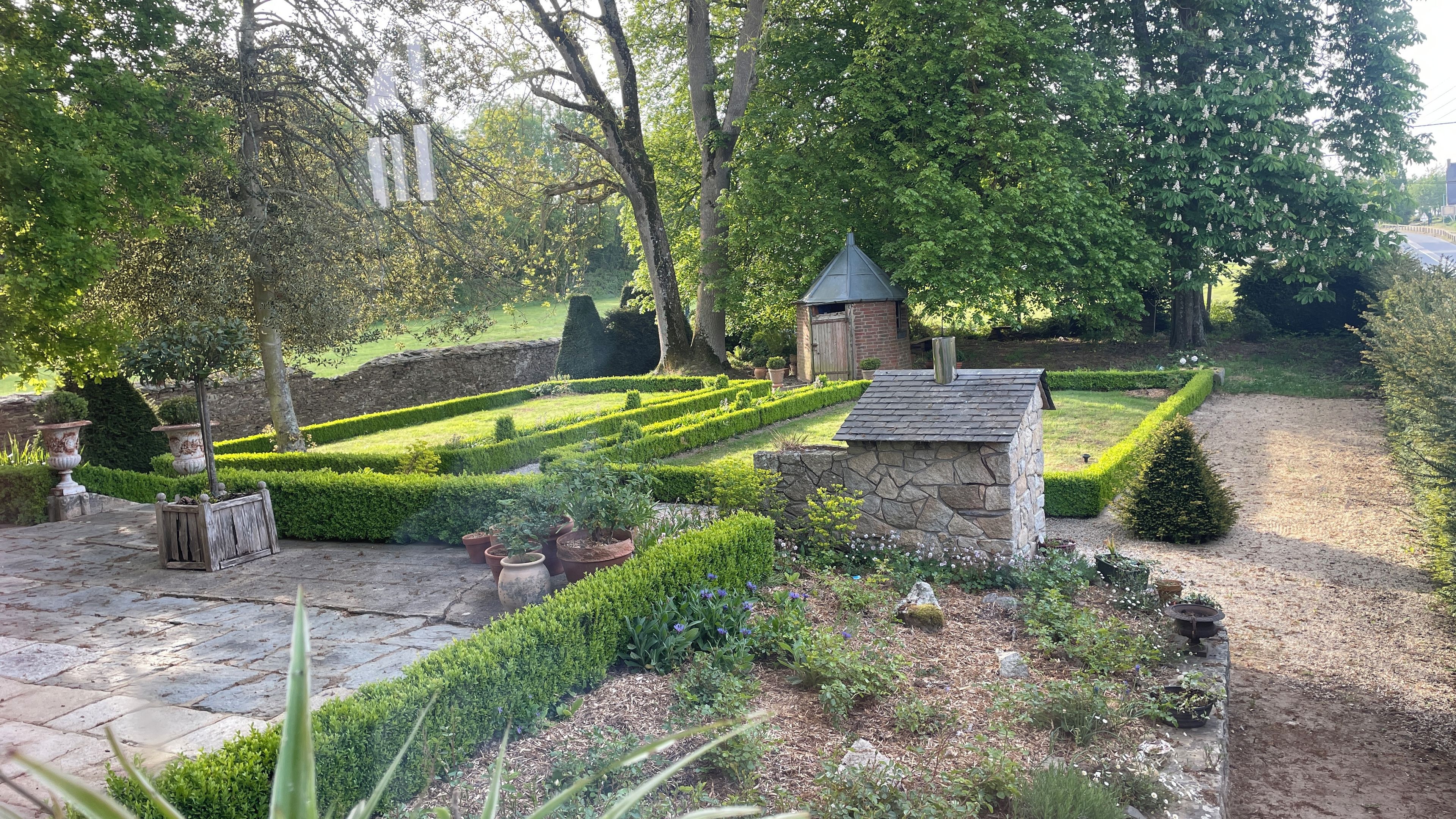 Ein gepflegter Garten mit einer Steinstruktur, ordentlich geschnittenen Hecken und verschiedenen Pflanzen.