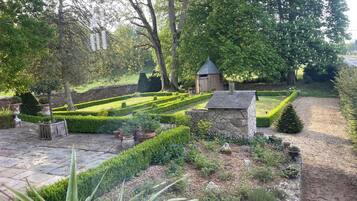 Ein gepflegter Garten mit einer Steinstruktur, ordentlich geschnittenen Hecken und verschiedenen Pflanzen.