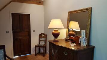 Een kamer met een houten deur, een kleine houten stoel, een kaptafel met spiegel en een tafel met een lamp.