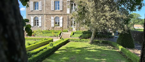 A stone building with arched windows and a well-manicured garden.