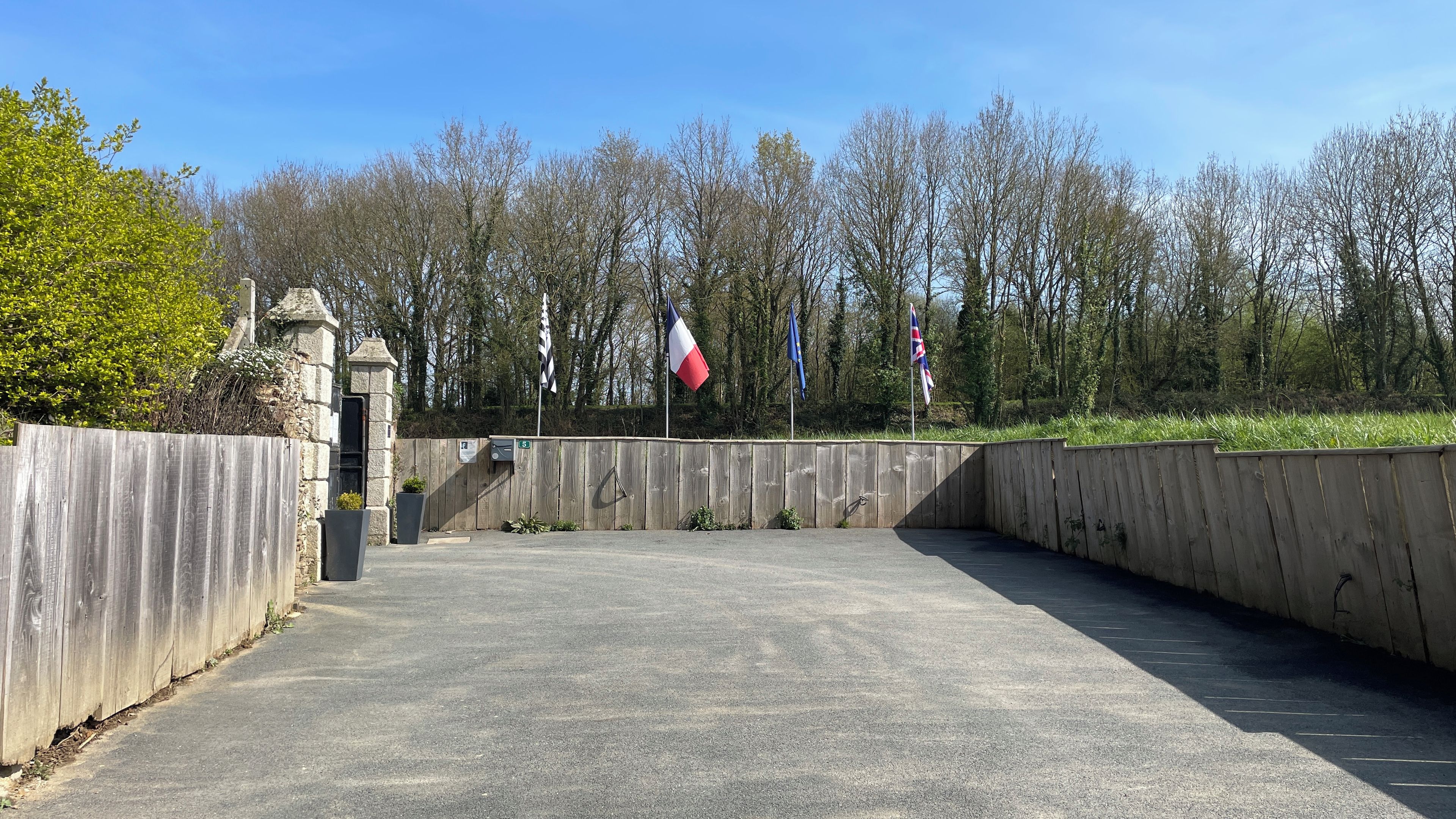 Een verharde oprijlaan met een stenen muur, een vlag en een houten omheining.