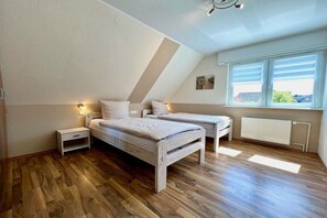 Ein Schlafzimmer mit schrägen Wänden, einem Bett, Nachttischen, einem Fenster mit Jalousien und einem Heizkörper.