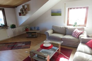 Ein Wohnzimmer mit Sofa, Couchtisch, Bücherregal und einem Fenster mit Blick.