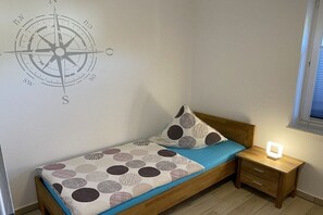 Ein Einzelbett mit gemustertem Bettbezug, ein Nachttisch mit Lampe und eine Kompass-Wanddekoration.