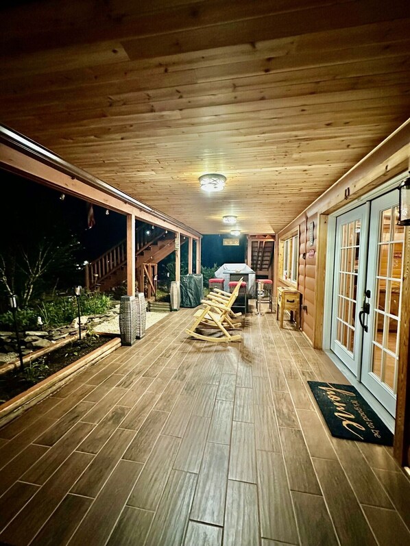 A covered outdoor area with a wooden floor, a barbecue grill, and a wooden swing set.