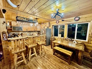 A rustic wooden interior with a bar area, wooden chairs, a dining table, and a refrigerator. - A Custom-Built Swiss-Style Luxury Mountain Retreat - Lower Level 2 BR Unit (Mount Jackson)