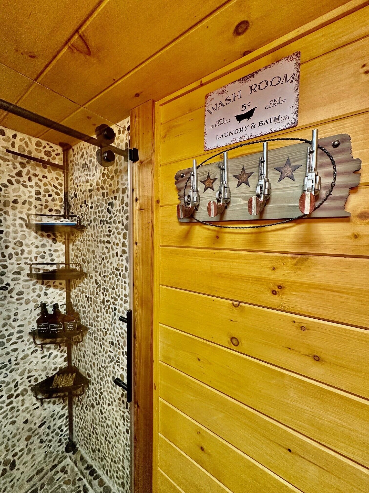 A rustic bathroom with a wooden door, a shower area with a stone wall, and a sign indicating a 5 cent fee for a hot shower, laundry, and bath.