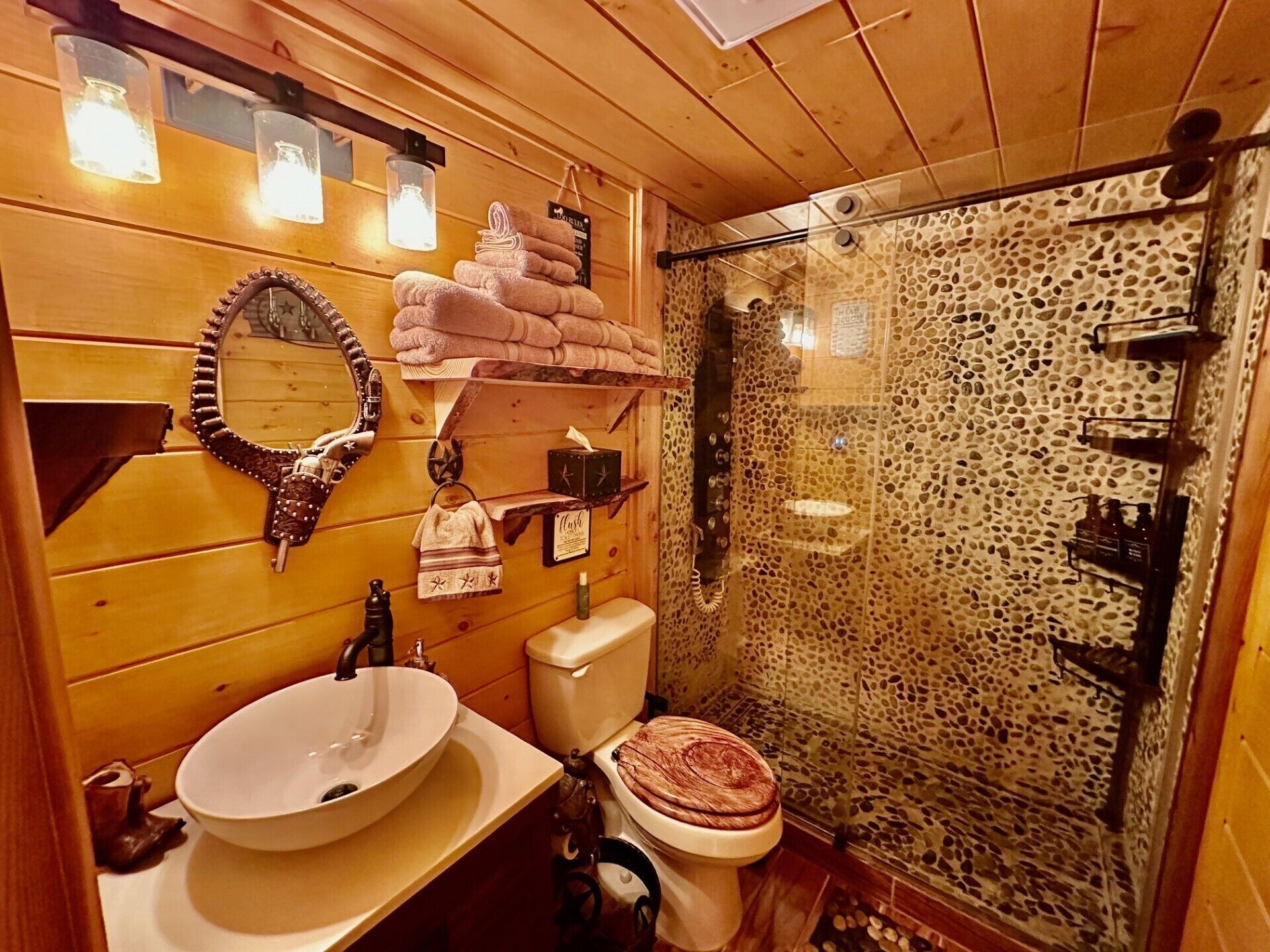 A wooden cabin bathroom with a round sink, a toilet, a mirror, and a shower enclosure.