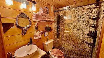 A wooden cabin bathroom with a round sink, a toilet, a mirror, and a shower enclosure.