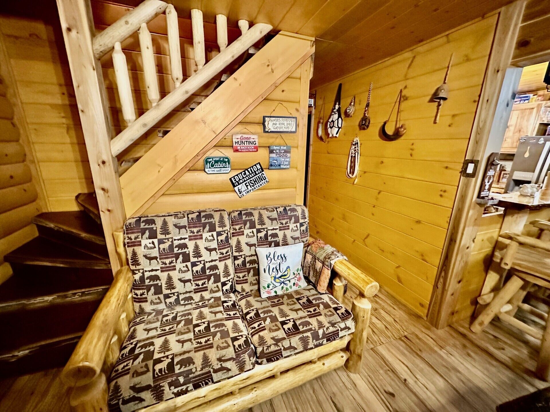 En stuga med träinredning, en trappa, en mönstrad soffa och fiskeutrustning som hänger på väggen.