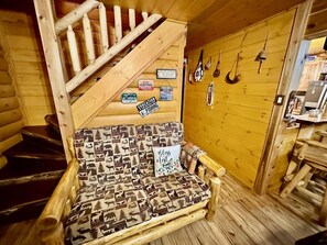 A cabin interior with a wooden staircase, a patterned sofa, and wall-mounted fishing equipment. - A Custom-Built Swiss-Style Luxury Mountain Retreat - Lower Level 2 BR Unit (Mount Jackson)