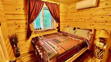 Quarto de cabana de madeira com uma cama grande, janela com cortinas, luminária no teto e aparelho de ar condicionado.
