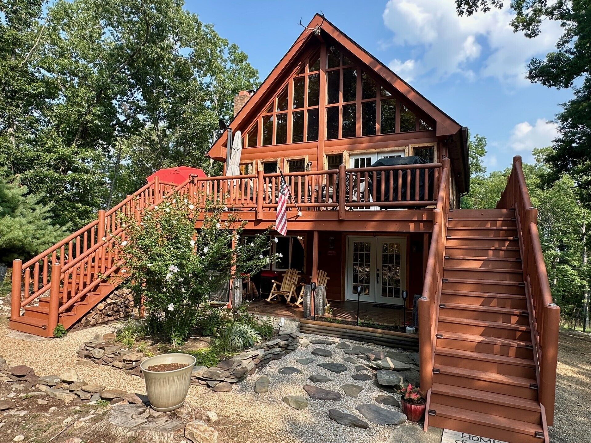 A two-story wooden cabin with a balcony, a stone staircase, and a flag.