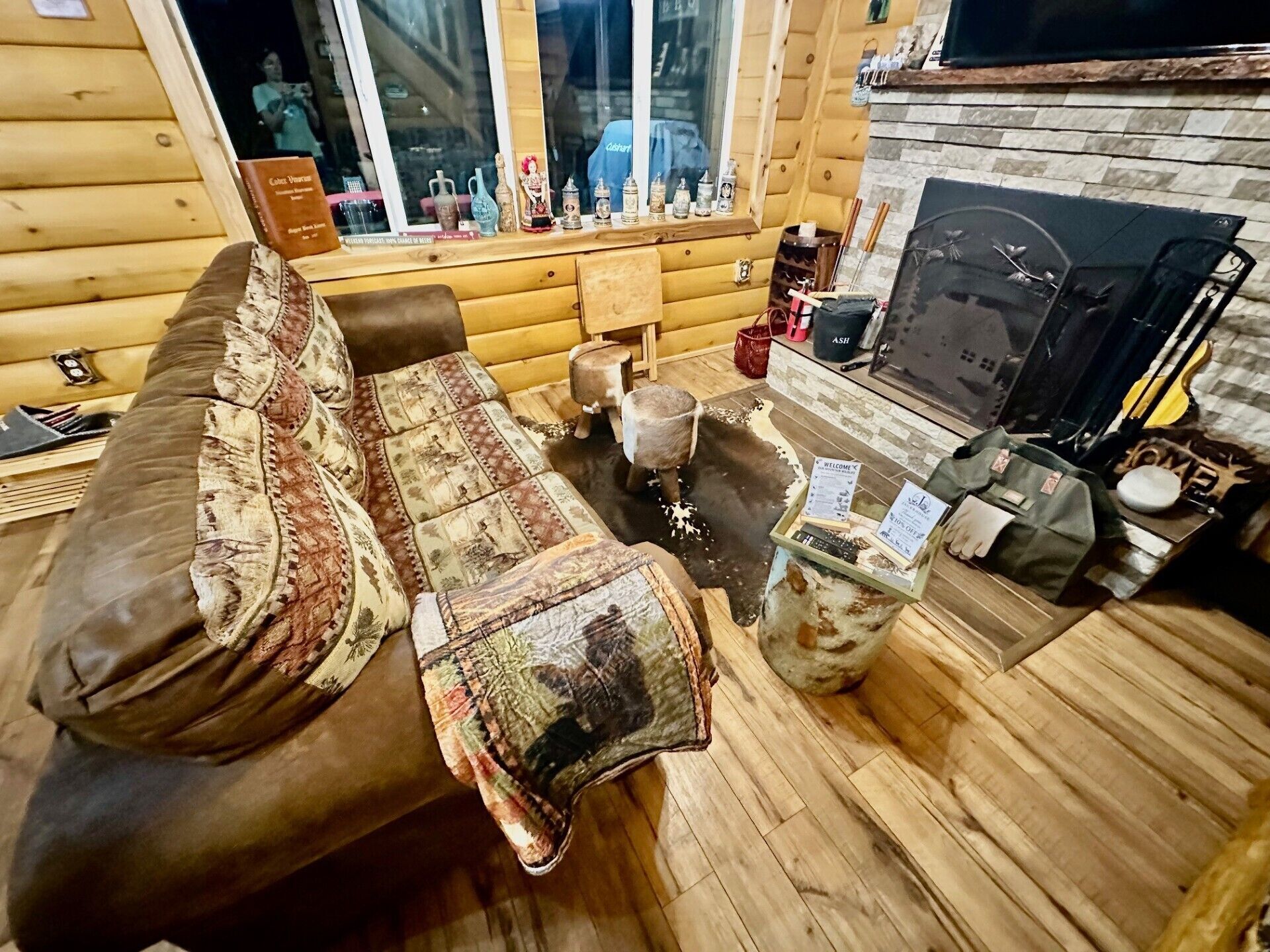 Ein gemütliches Blockhaus-Interieur mit einer Couch, einem kleinen Hocker, einem Kamin und verschiedenen Dekorationselementen.