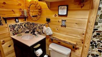 Ein Badezimmer aus Holz mit einer Wand aus Steinmosaik, einem Waschbecken, einer Toilette und Regalen mit Handtüchern.