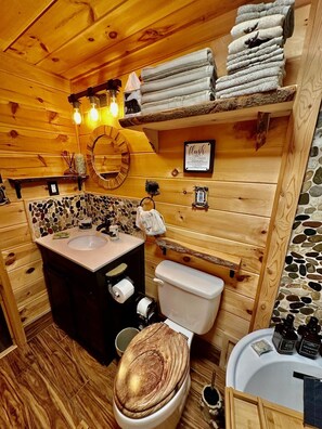 A wooden bathroom with a stone mosaic wall, a sink, toilet, and shelves with towels. - A Custom-Built Swiss-Style Luxury Mountain Retreat - Lower Level 2 BR Unit (Mount Jackson)