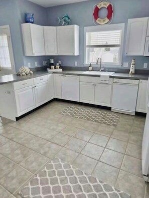 A kitchen with white cabinets, a tiled floor, and a decorative rug. - Bayside Ortley Retreat 6 Badges And Parking (Seaside Heights)