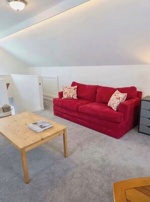 Ein rotes Sofa mit gemusterten Kissen, ein Holztisch und eine graue Kommode.