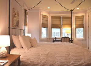 Une chambre à coucher avec un lit à baldaquin, une table de chevet, une lampe et une fenêtre donnant sur un beau paysage.