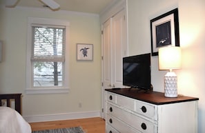 A bedroom with a bed, a dresser, a television, and a window with blinds.