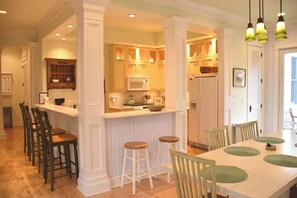 Une cuisine avec des meubles blancs, un îlot central, des tabourets de bar et une table à manger avec des chaises.